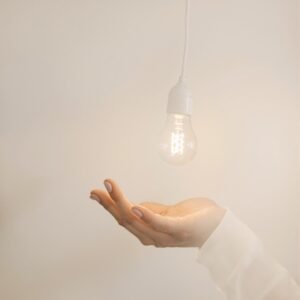 Une main ouverte sous une ampoule allumée suspendue, dans un décor minimaliste et lumineux, symbolisant une idée ou une révélation inspirante.