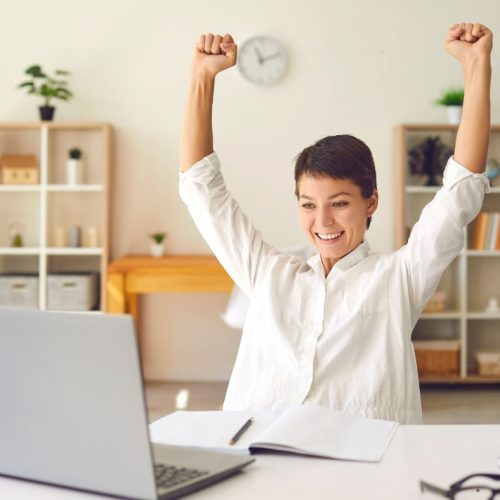 Femme entrepreneure célébrant un succès devant son ordinateur, symbolisant la liberté et l’autonomie dans le travail en solo.