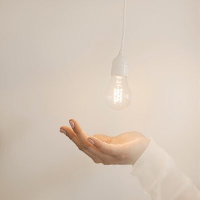 trouver-pourquoi Une main ouverte sous une ampoule allumée suspendue, dans un décor minimaliste et lumineux, symbolisant une idée ou une révélation inspirante.